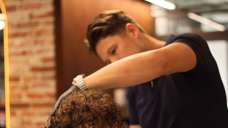 Marcin, barber Złotobrody, strzyże kręcone włosy klienta w salonie